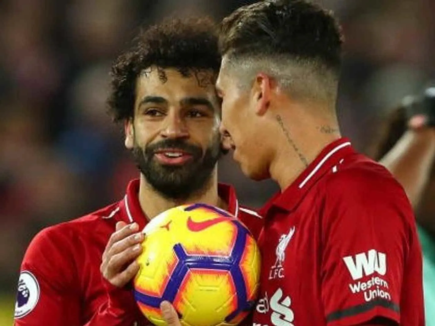 The photo shows Mohamed Salah and Roberto Firmino holding a football during a Liverpool game against Arsenal.